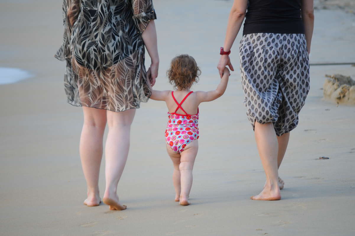 A baby walking between two women Baby between two women